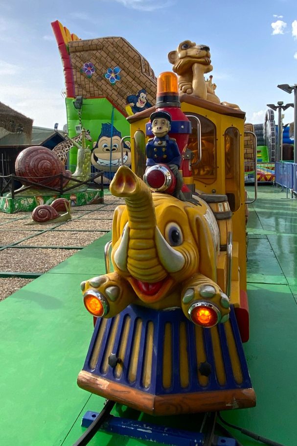 El elefante locomotora Tren infantil amarillo con elefante y figuras de colores en un parque de atracciones.