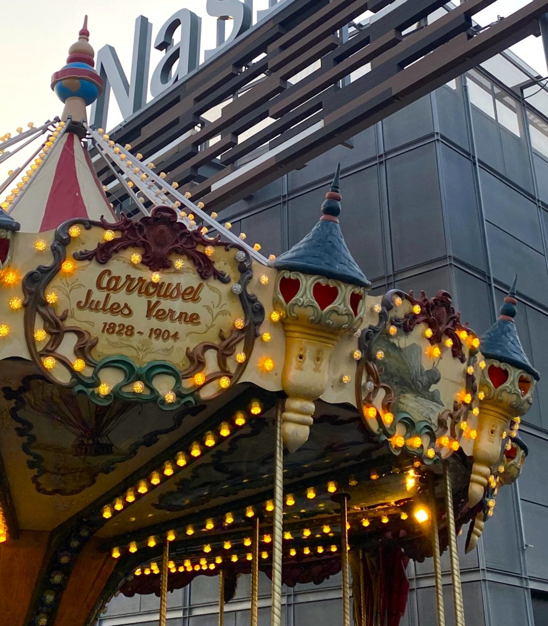 Carrusel iluminado frente al edificio de Nassica, con personas disfrutando.