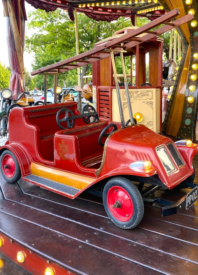 Camión de bomberos Coche de feria rojo con ruedas negras, expuesto en un entorno festivo.