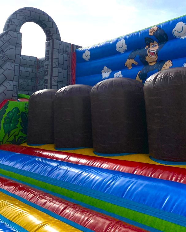 Desafío del gorila Inflable colorido con obstáculos y figura de un gorila en un fondo de muro de piedra.