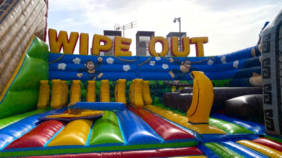 Más pruebas, más diversión Inflable colorido de "Wipe Out" con obstáculos y letras grandes en un entorno festivo.