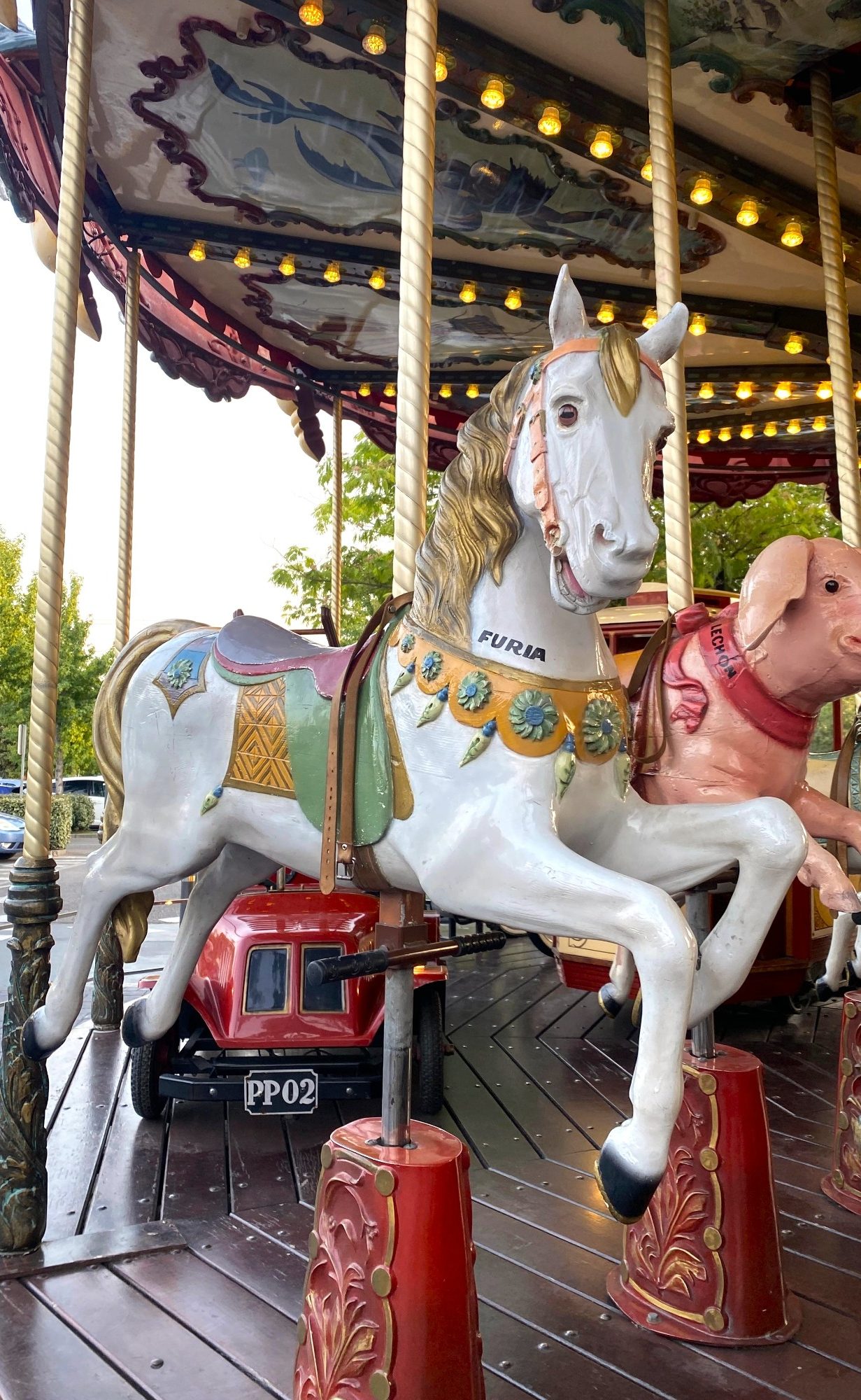 Caballo del Carrusel Caballo de carrusel decorado con un collar multicolor y figura de perro al fondo.