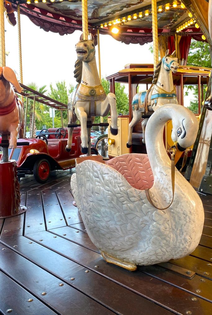 Cisne y caballos Cisne decorativo de un carrusel con caballos y un coche rojo de fondo.